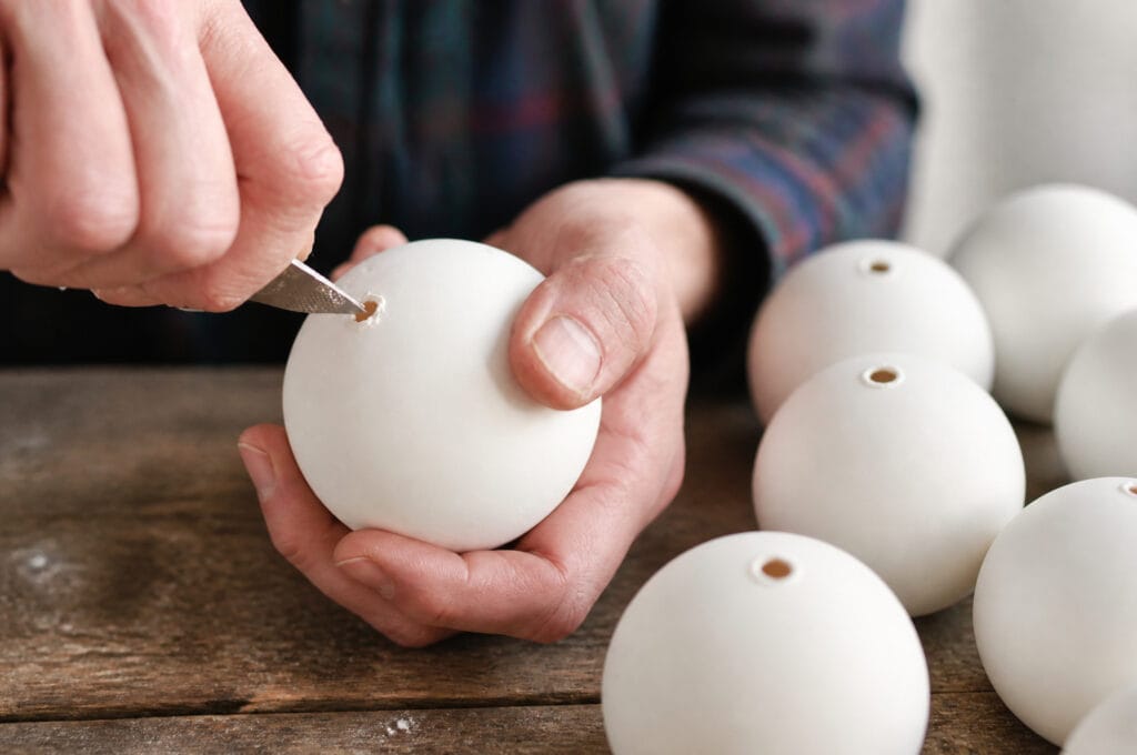 Craft knife opening a hole in a white Christmas bauble for floral insertion