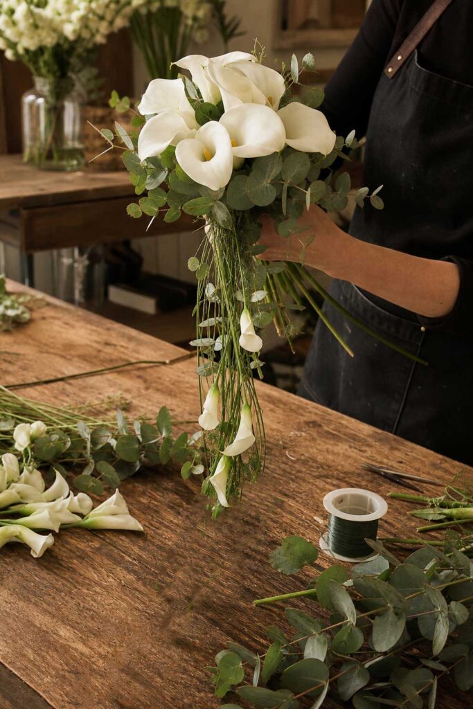 Florist hands building cascading calla lily bouquet with eucalyptus foliage