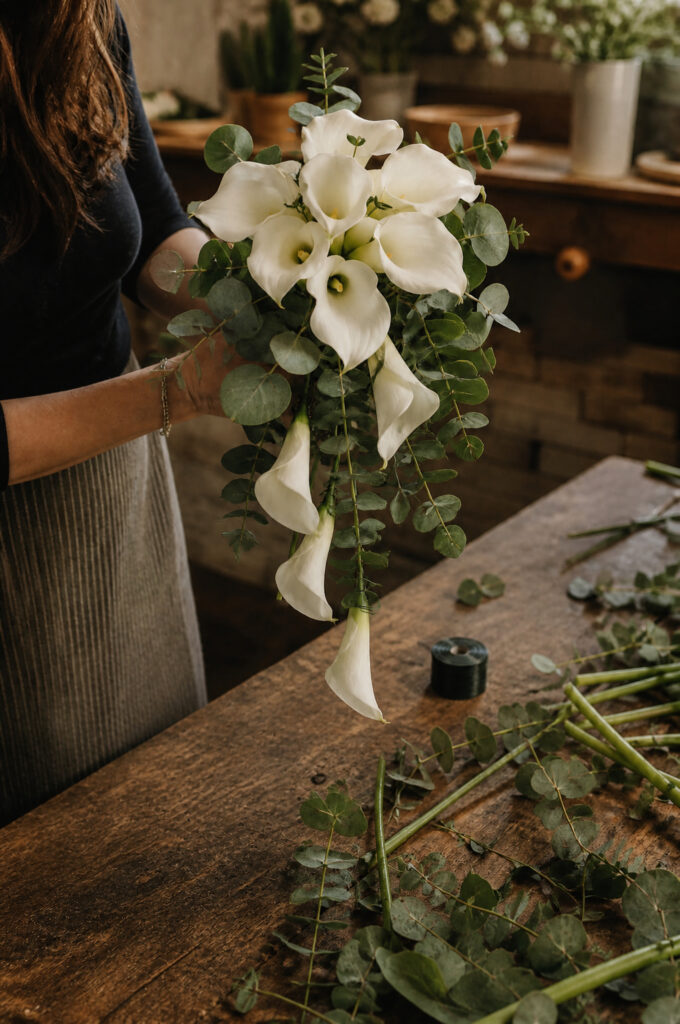 Florist hands building cascading calla lily bouquet with eucalyptus foliage