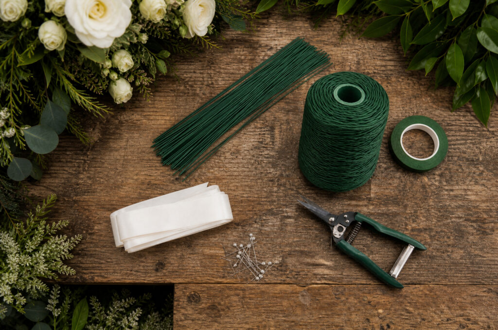 Floral wire, floral tape, ribbon, pearl pins and scissors laid out on a wooden worktable