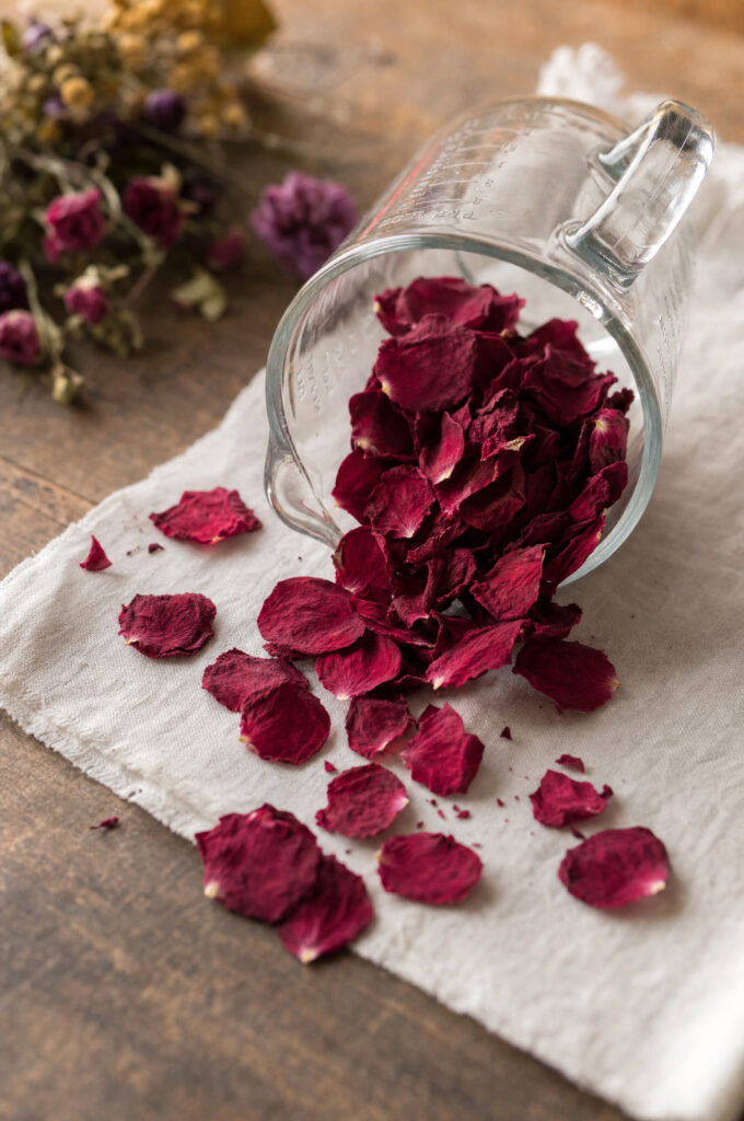 A measuring cup of freeze-dried rose petals being poured onto a square foot of white fabric on a workbench