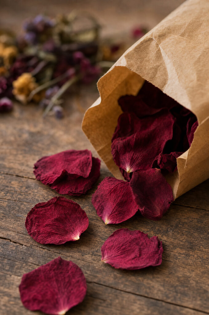 Freeze-dried rose petals arranged in a small pile on a florist's workbench beside an open kraft paper bag