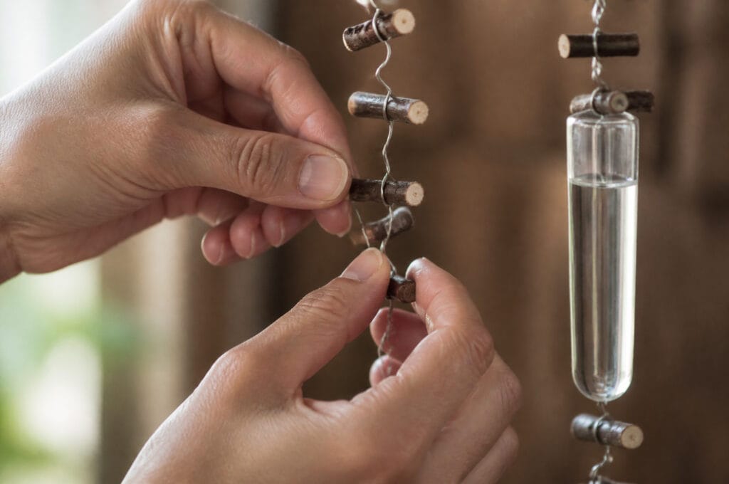Florist's hands twisting wire to attach a twig and water tube while building a flower curtain garland