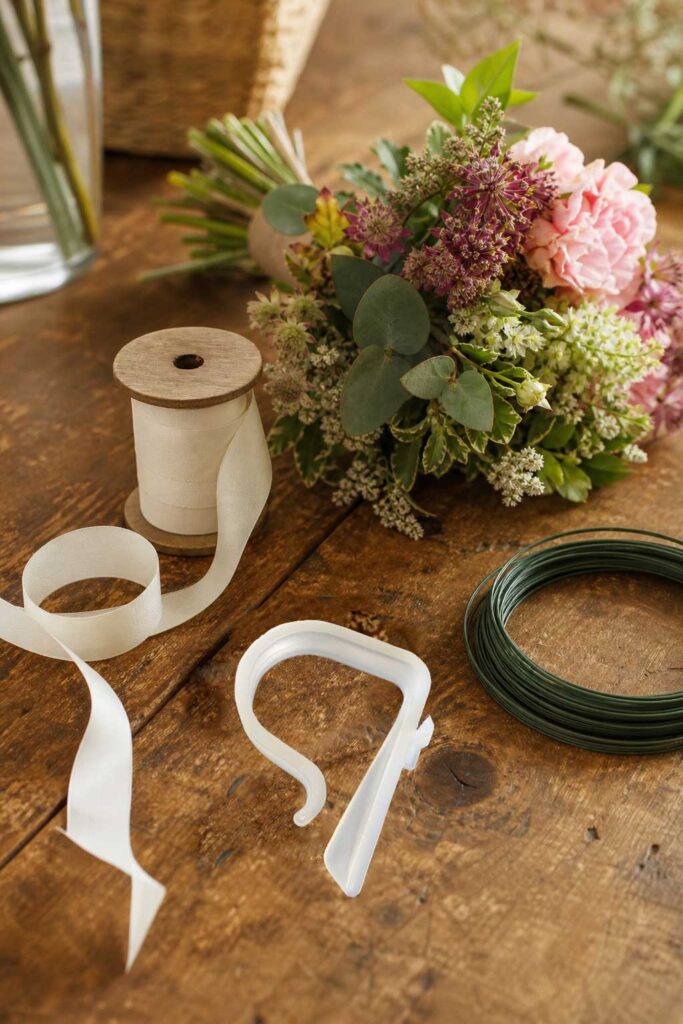 Pew clip, floral wire, and ribbon laid out on a wooden surface beside a small floral arrangement