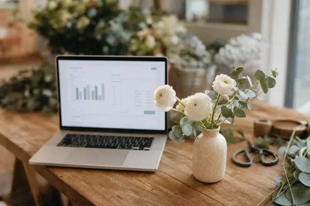 Laptop open to a wedding cost estimator tool beside fresh flowers on a wooden table