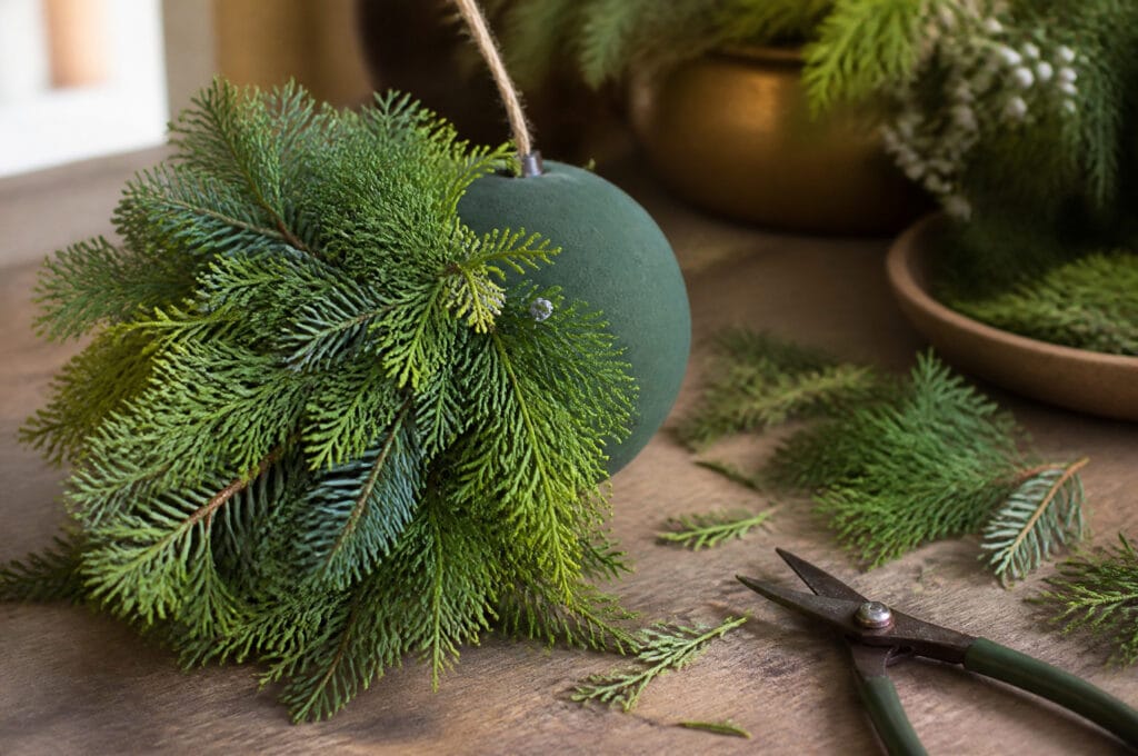 Partially assembled Christmas kissing ball showing evergreen sprigs inserted into foam