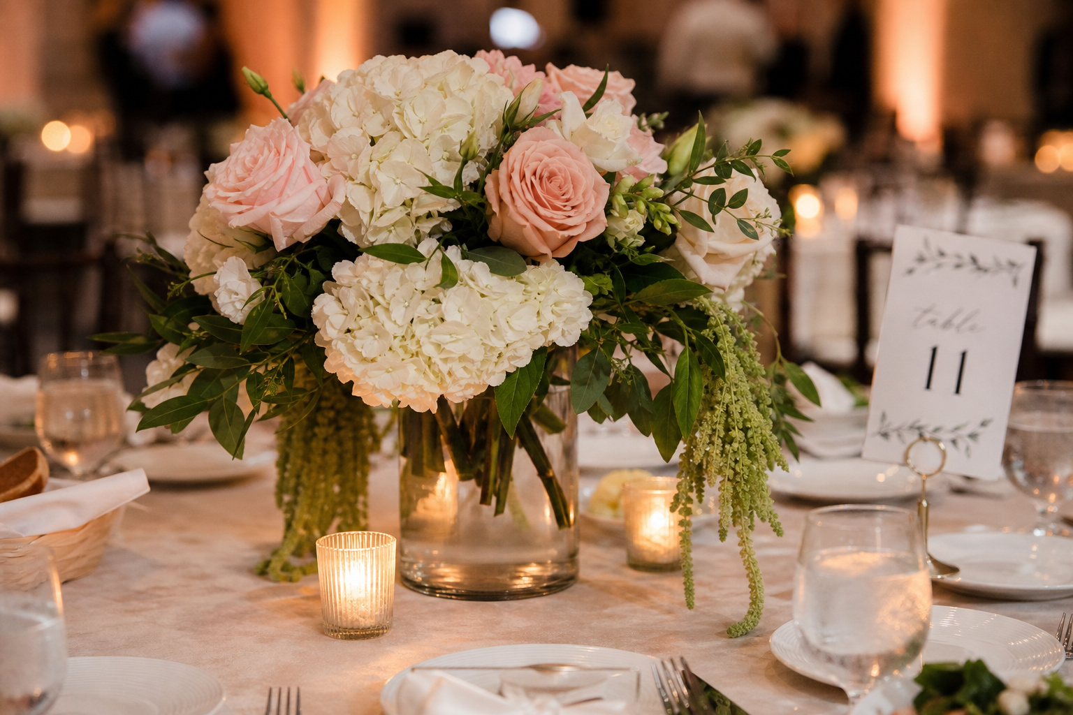 Wedding reception centerpiece of white hydrangeas and blush roses on a guest table