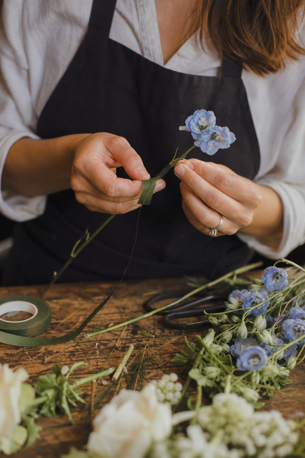 Florist's hands wiring a small flower with floral wire and tape on a wooden bench