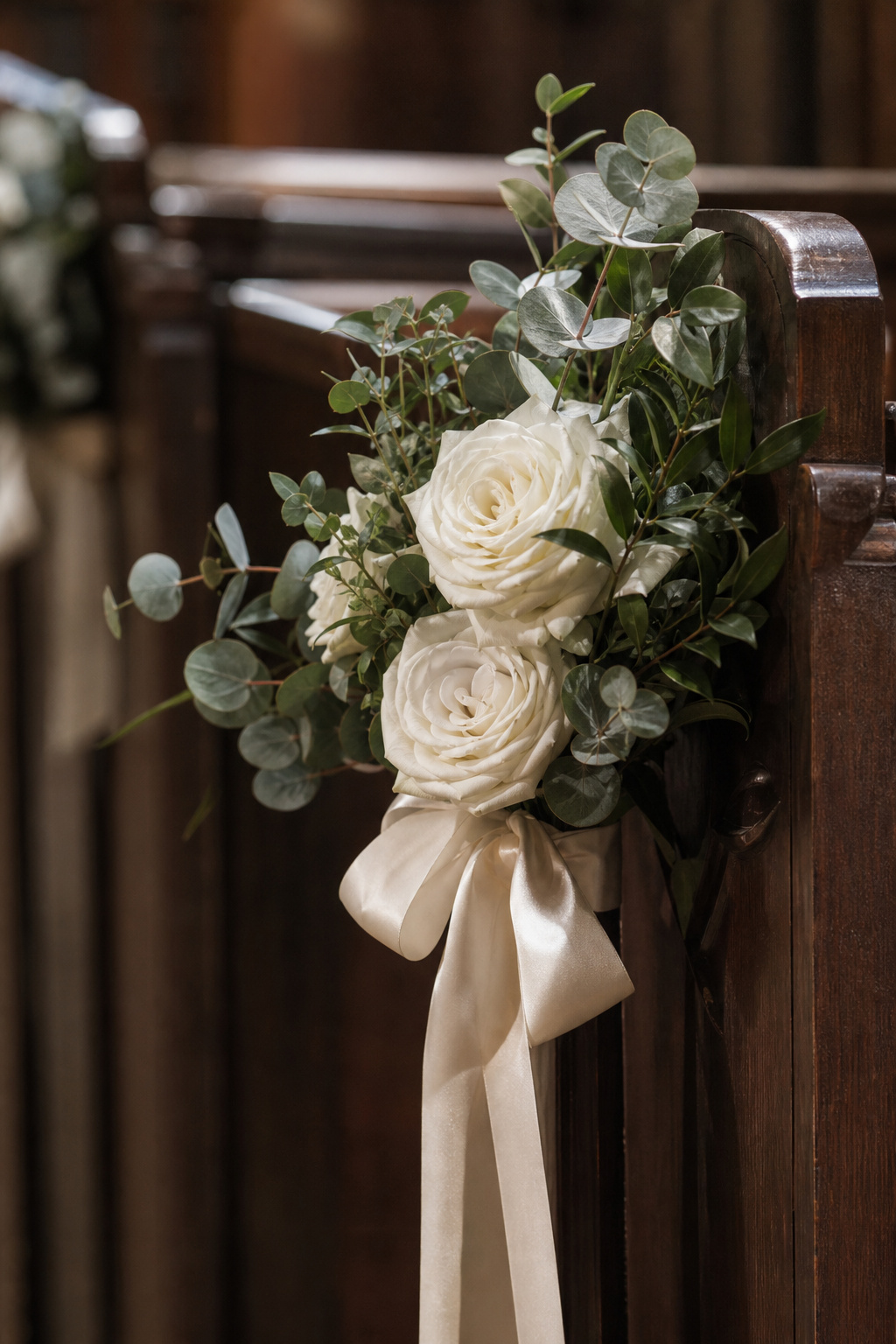 Silk flower pew end arrangement with fresh eucalyptus mixed in on a church pew