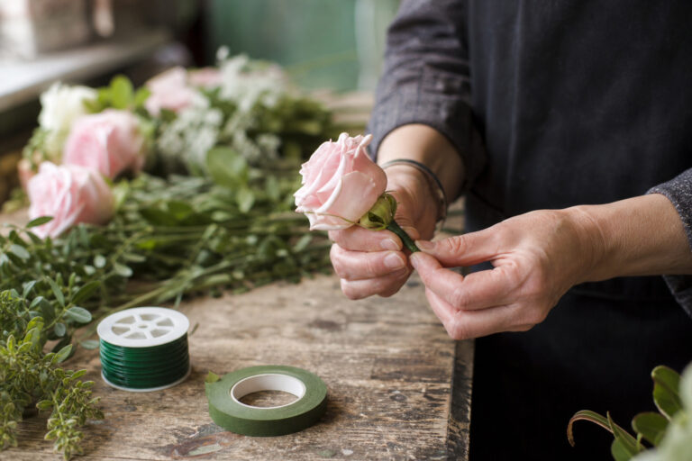 Florist wiring a rose for a corsage on a wooden worktable