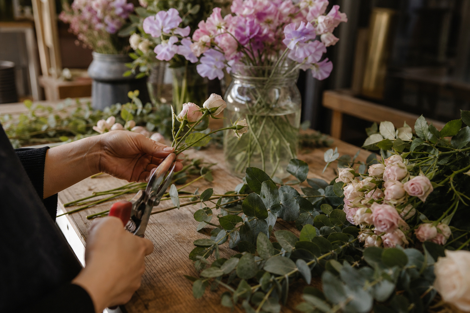 Florist hands trimming sweet pea stems at a wooden worktable