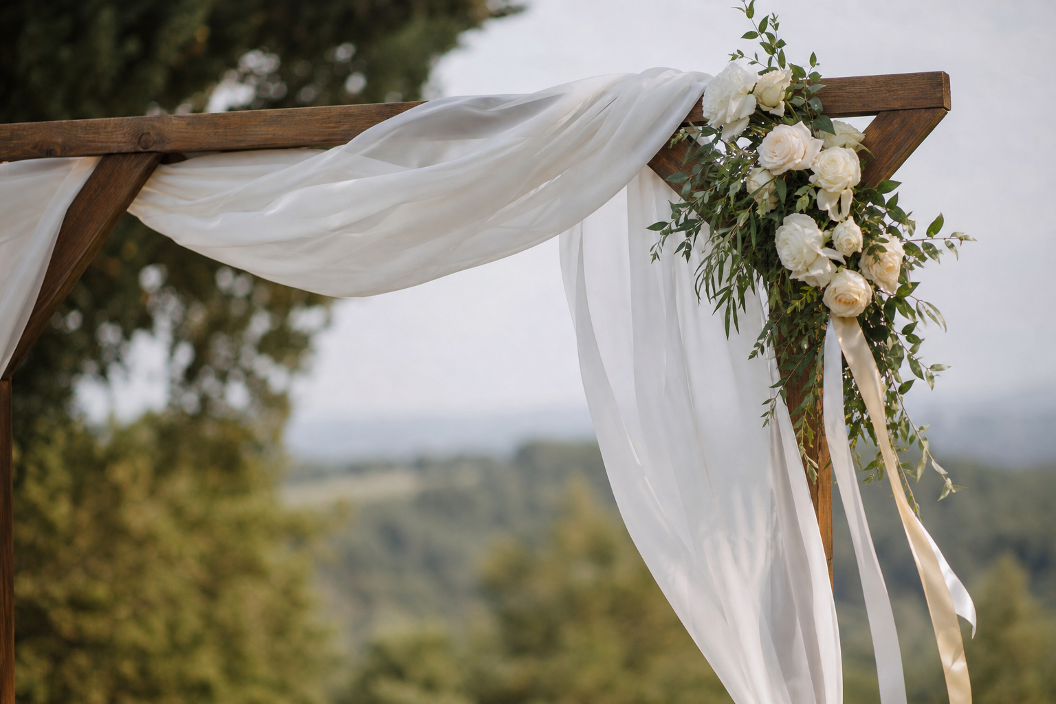 White chiffon fabric and satin ribbon draped over a simple wedding arch