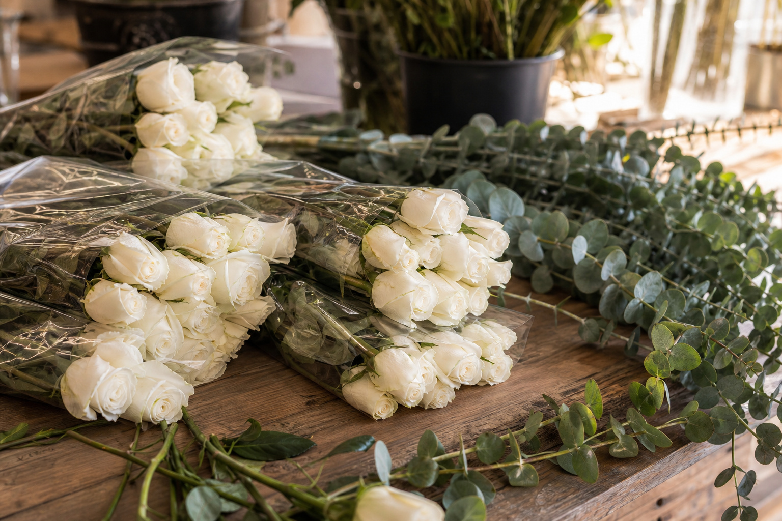 Bundles of bulk white roses and eucalyptus stems on a wooden florist worktable