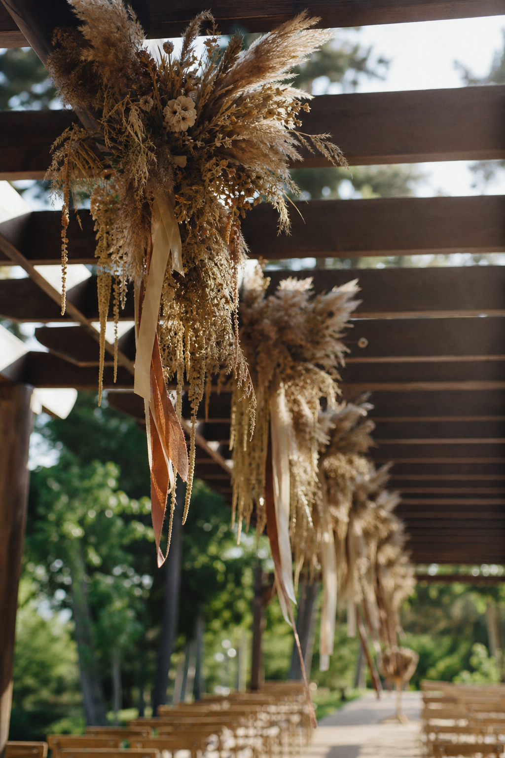 Hanging dried flower and pampas grass bundles above a wedding ceremony aisle pergola