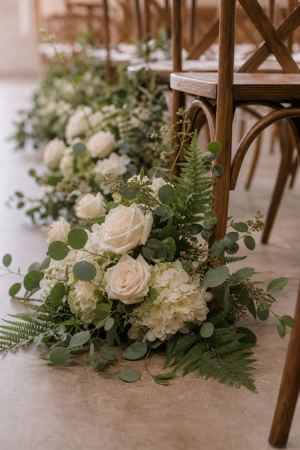 Silk white rose and hydrangea ground arrangements beside wedding ceremony chairs