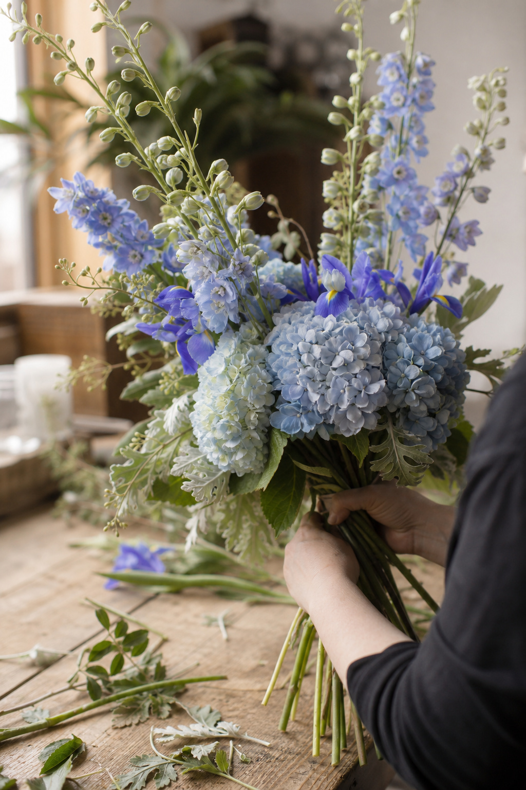 Florist hand-tying a blue wedding bouquet with spiral stem technique on a worktable