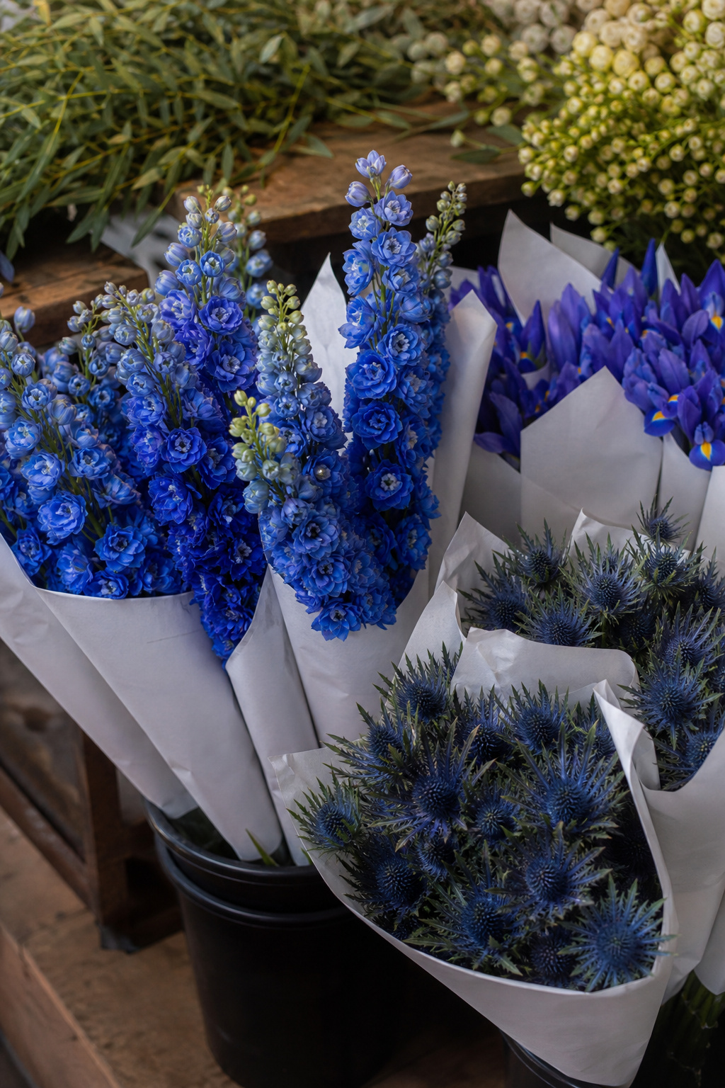 Bunches of blue delphinium and iris stems in water buckets at a wholesale flower market
