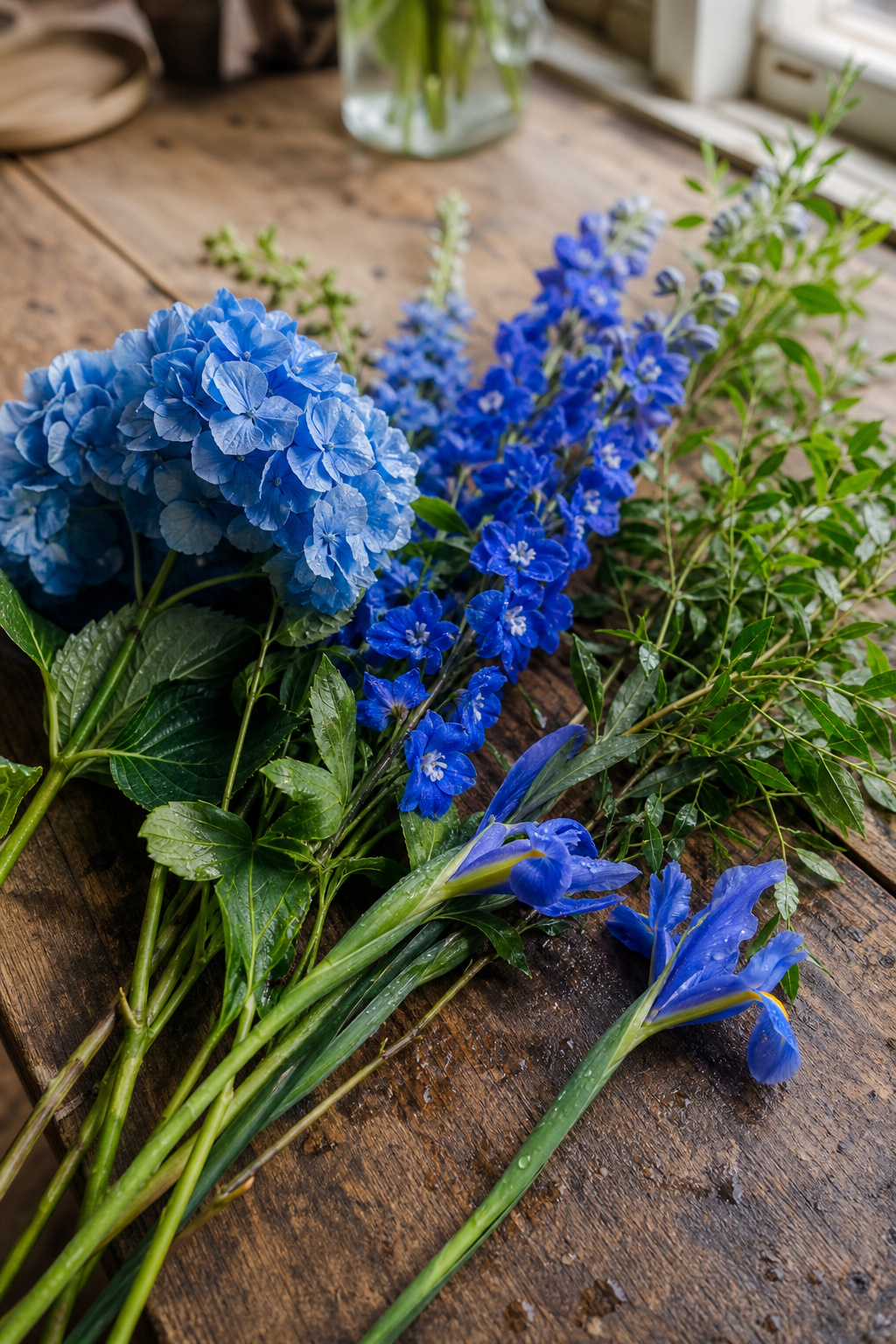 Blue hydrangea, delphinium spikes, and iris blooms arranged on a florist's worktable
