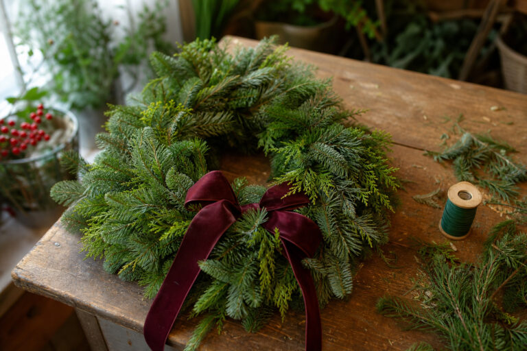 Fresh Christmas wreath with mixed greenery and wired ribbon bow on a florist's worktable