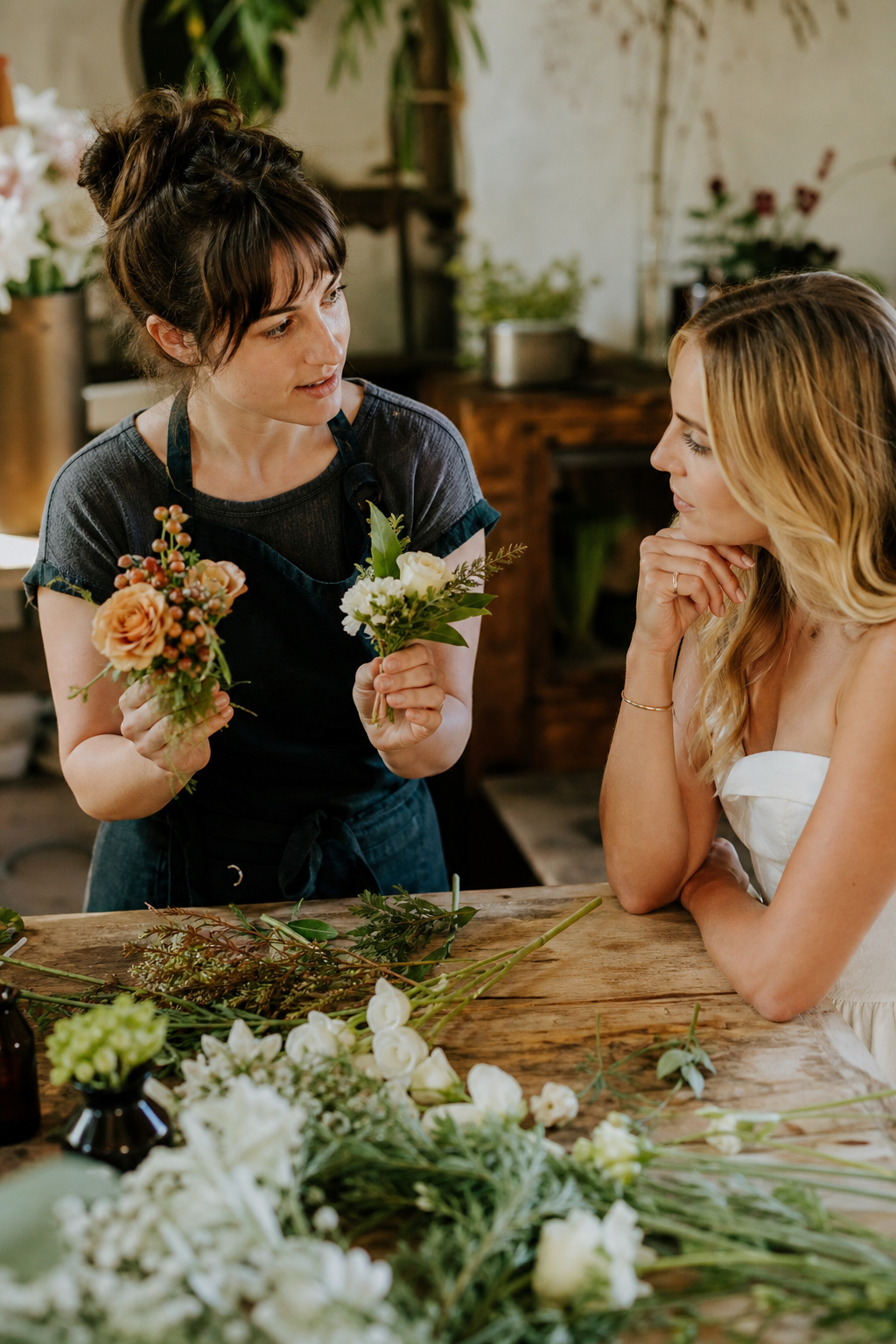 Florist showing seasonal flower options to a bride at a wooden worktable