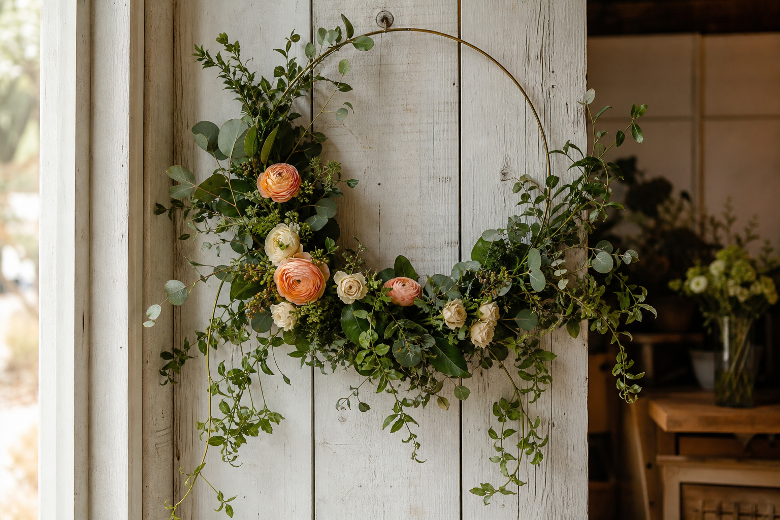 Finished floral hoop with eucalyptus, huckleberry, and ranunculus hanging on a white wall