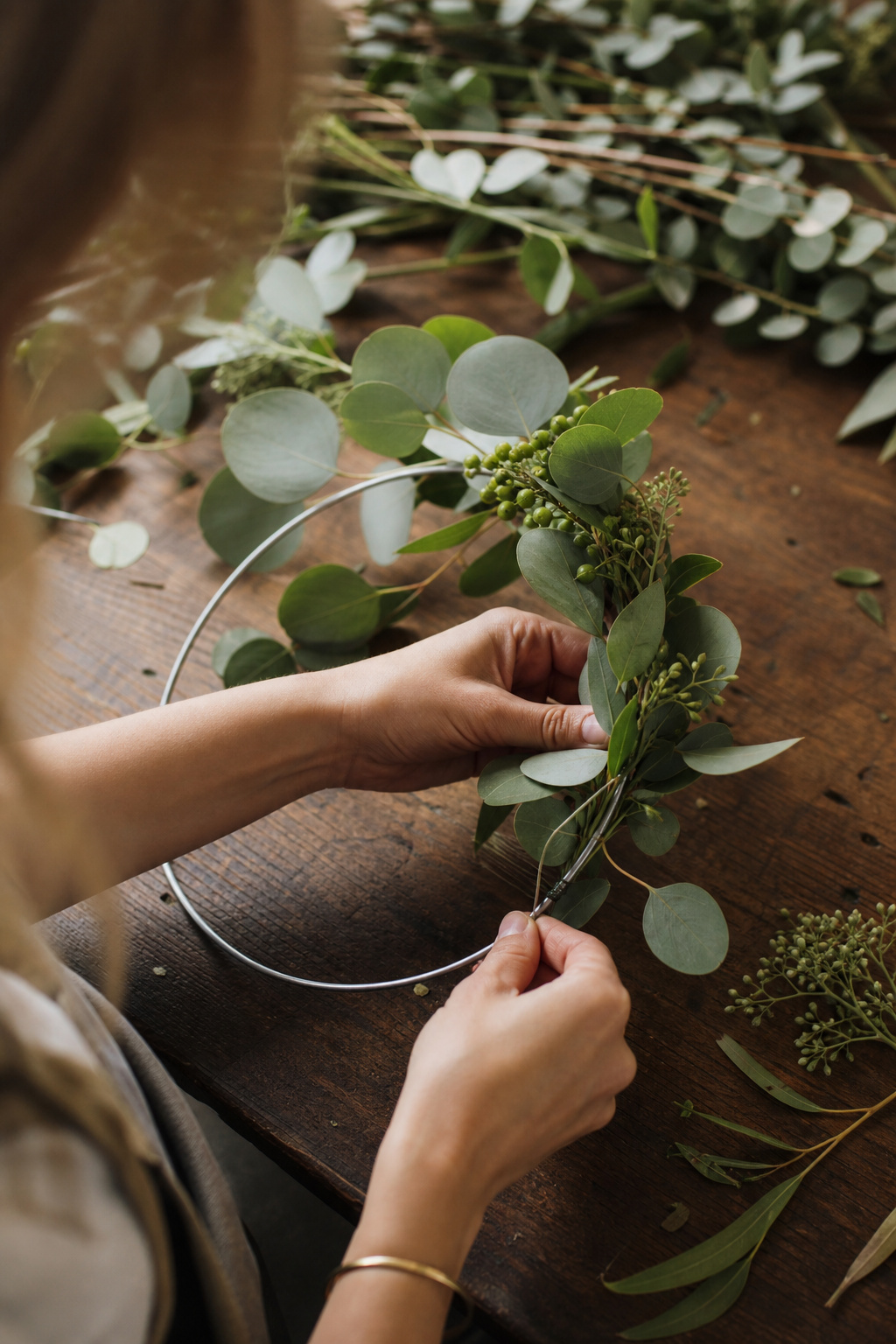 Hands winding silver dollar eucalyptus and huckleberry around a metal floral hoop