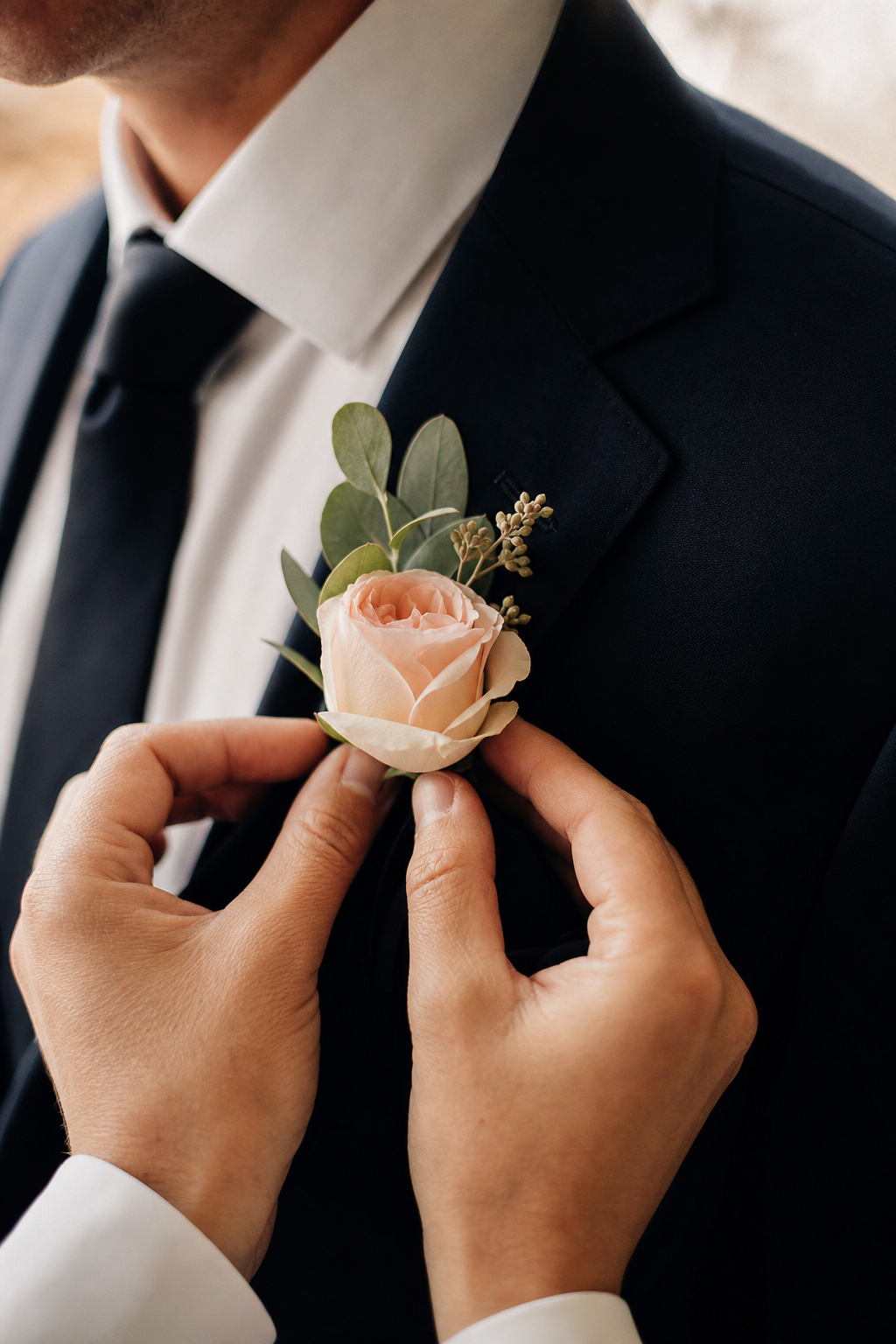 Florist pinning a boutonniere onto a groom's lapel before a wedding ceremony