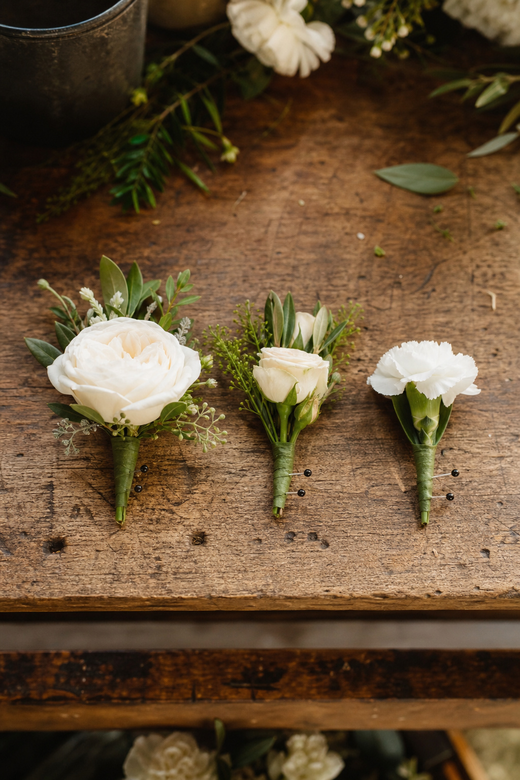 Groom and groomsmen boutonnieres lined up on a wooden surface showing visual hierarchy