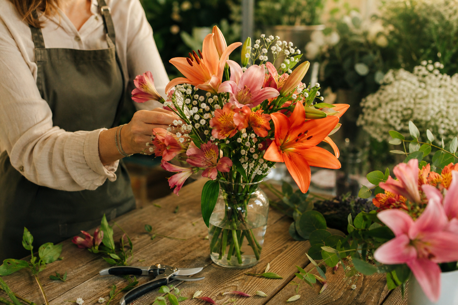 Florist arranging freshly cut garden flowers including Asiatic lilies and alstroemeria in a glass vase