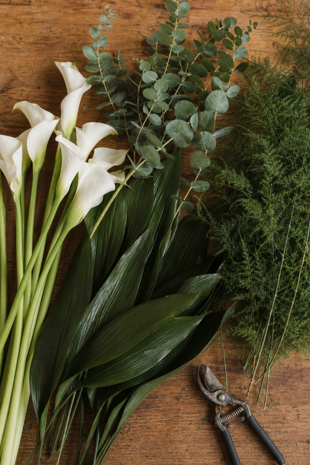 Fresh calla lilies, eucalyptus and aspidistra leaf arranged on a florist worktable