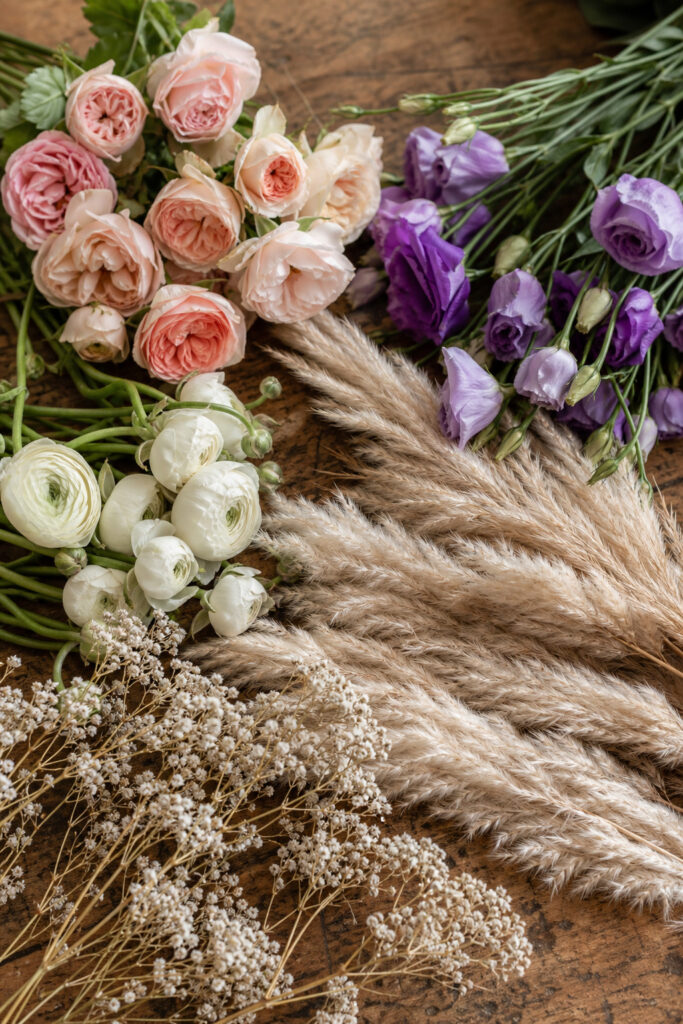 Garden roses, ranunculus, dried pampas grass and lisianthus arranged loosely on a florist worktable