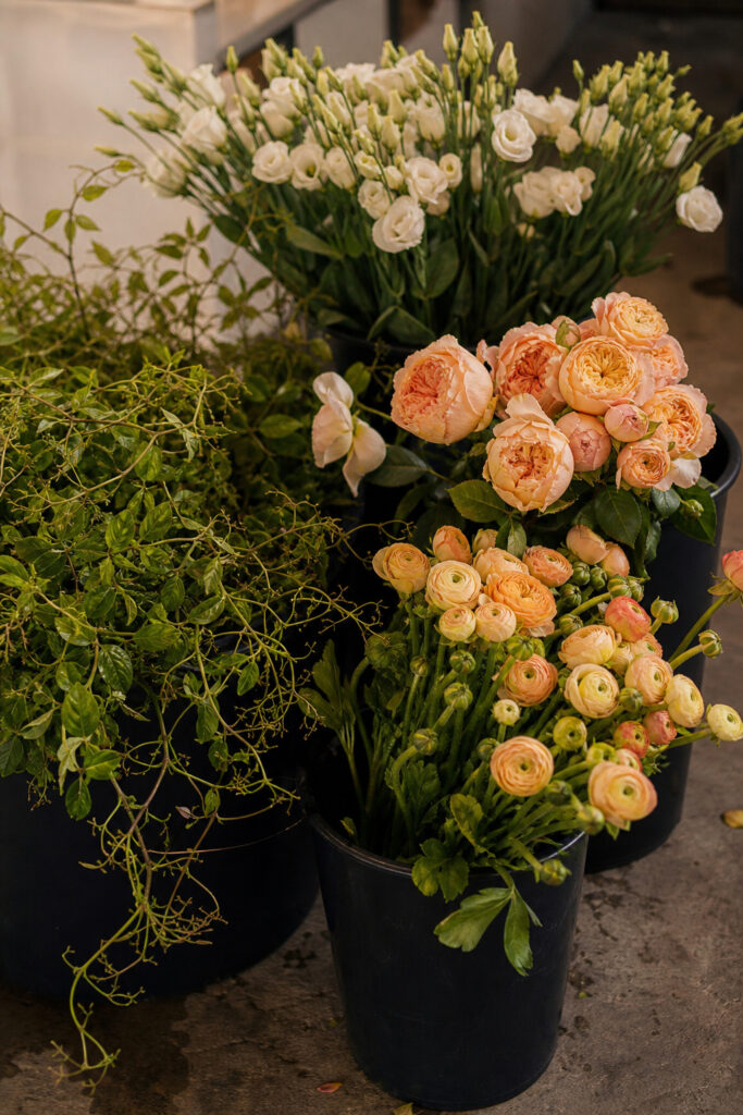 Cut flower stems in water buckets on a florist workroom floor being conditioned before assembly