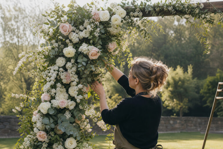Florist arranging a lush wedding ceremony arch with roses and eucalyptus