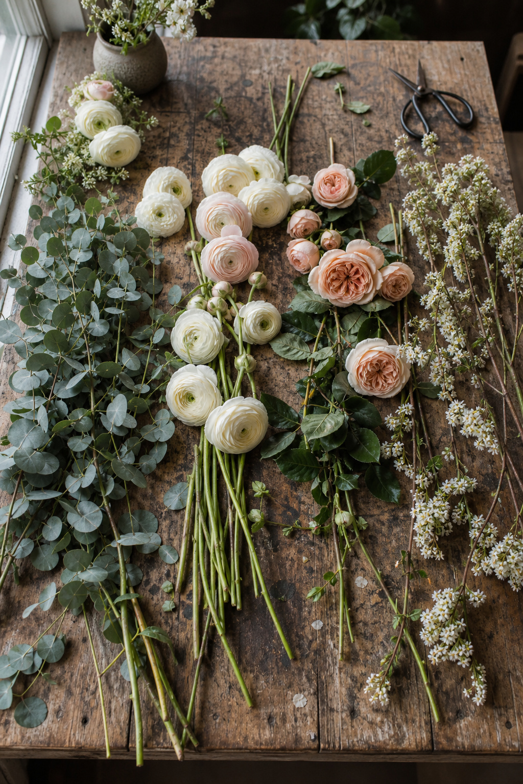 Bunches of ranunculus, eucalyptus, and roses laid out for a ceremony arch