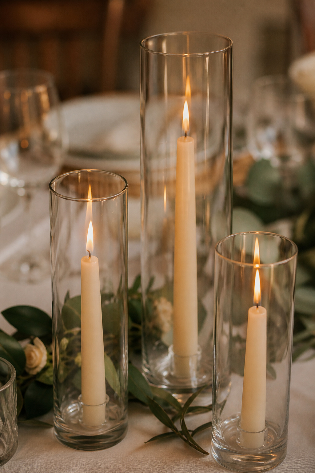 Taper candles enclosed in glass hurricane shades on a reception table
