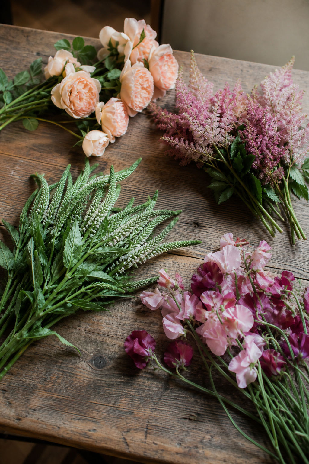 Garden roses, astilbe, veronica, and sweet peas laid out separately on a wooden bench