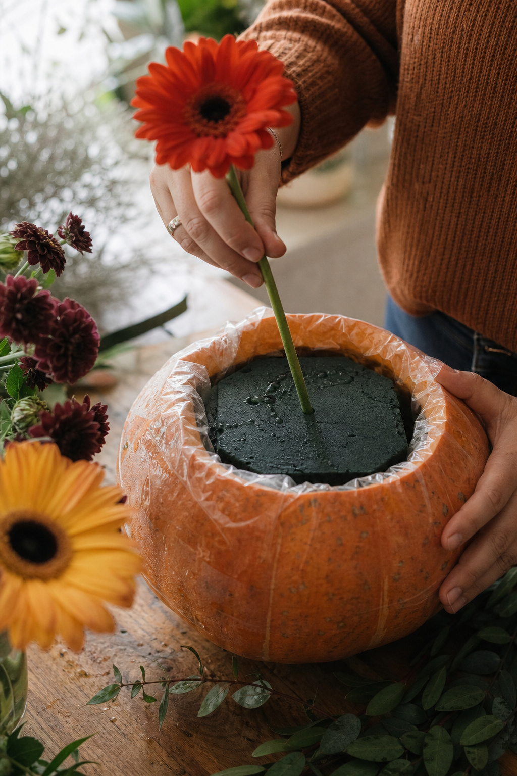 Soaked floral foam brick placed inside a lined pumpkin cavity with flowers being inserted