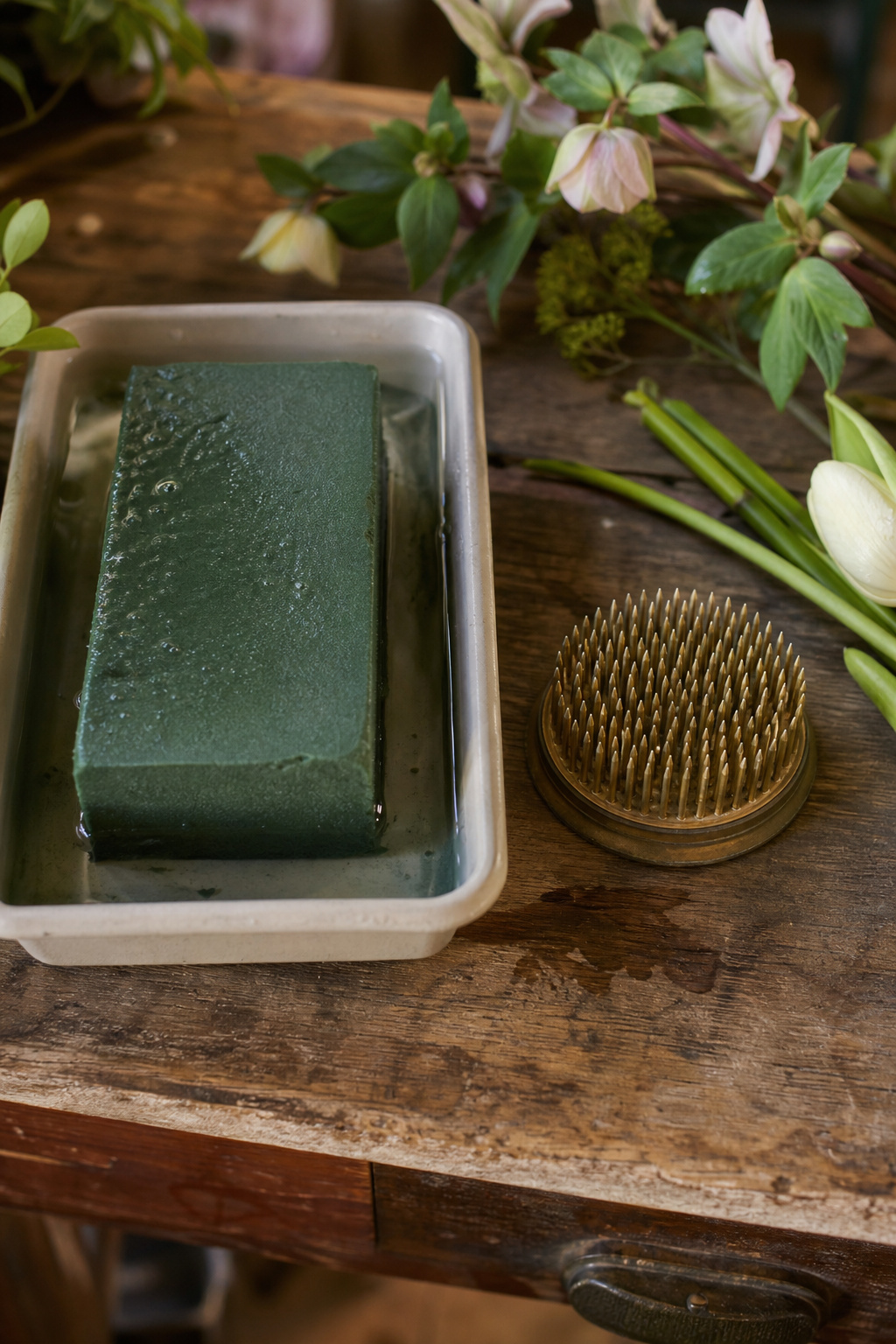 Floral foam brick soaking in water next to a pin-style flower frog on a florist's worktable