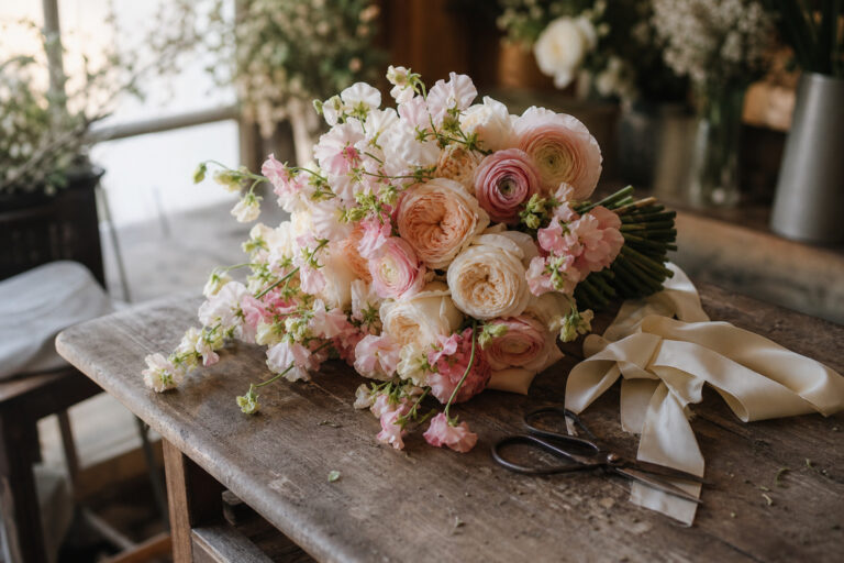Hand-tied bridal bouquet of garden roses and ranunculus resting on a wooden florist worktable