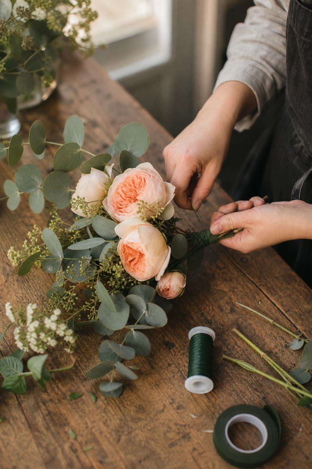Hands wiring garden rose stems together to build a corner floral swag