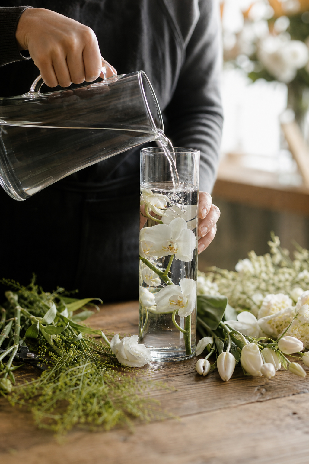 Hands pouring distilled water into a glass vase with a submerged orchid