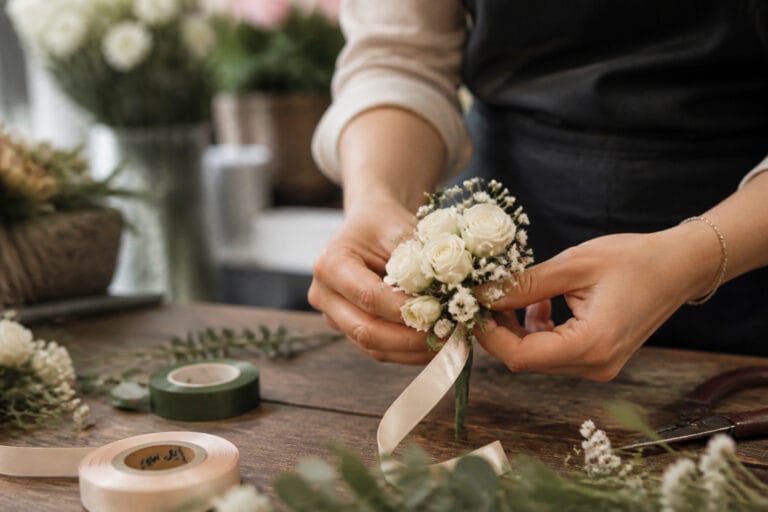 Florist assembling a white spray rose wrist corsage on a worktable