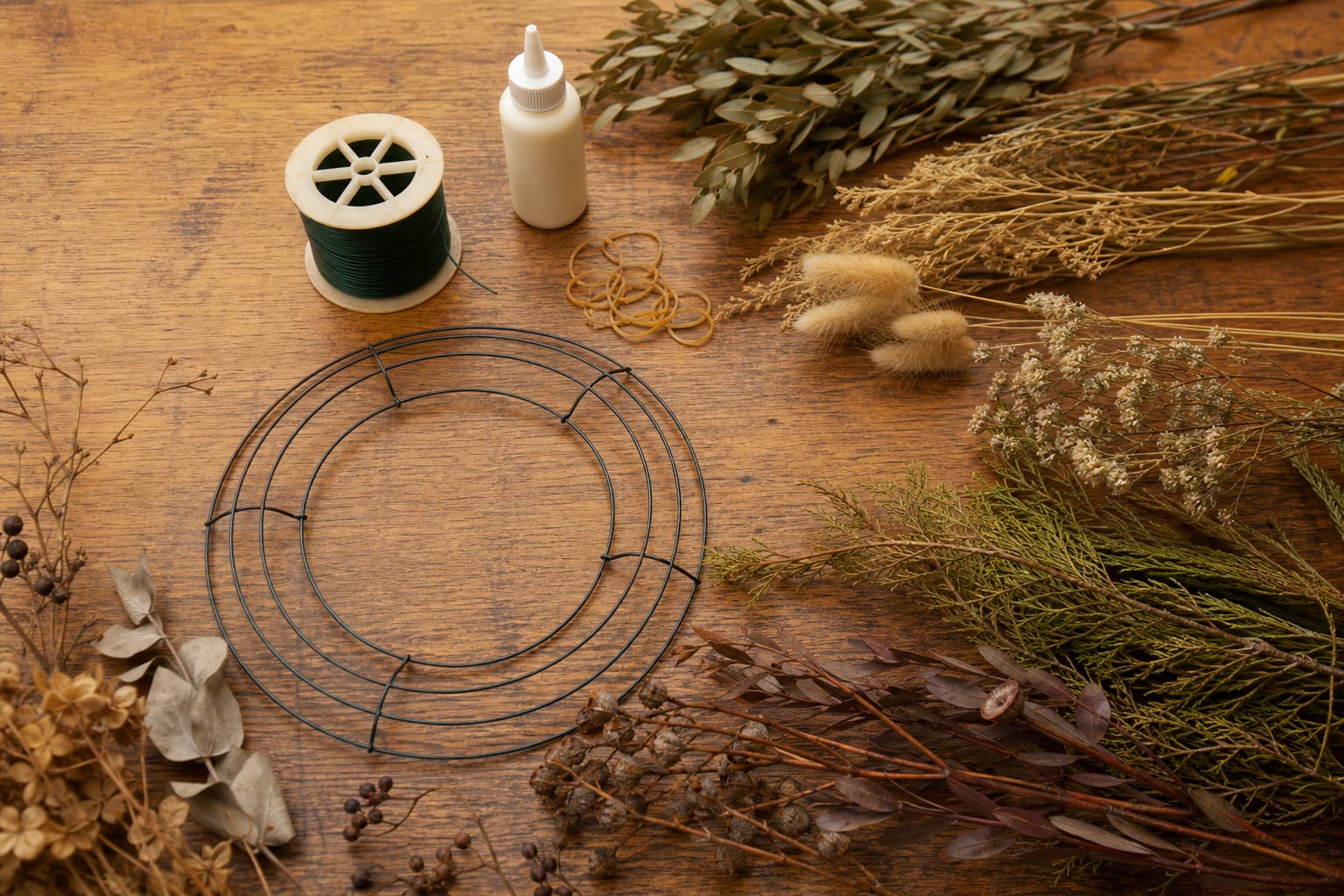 Wreath-making supplies including wire frame, paddle wire, floral glue, and rubber bands on a worktable