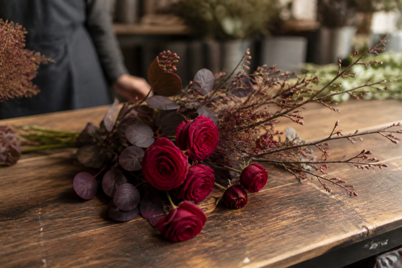 A short bundle of dark roses and plum branches ready for arranging
