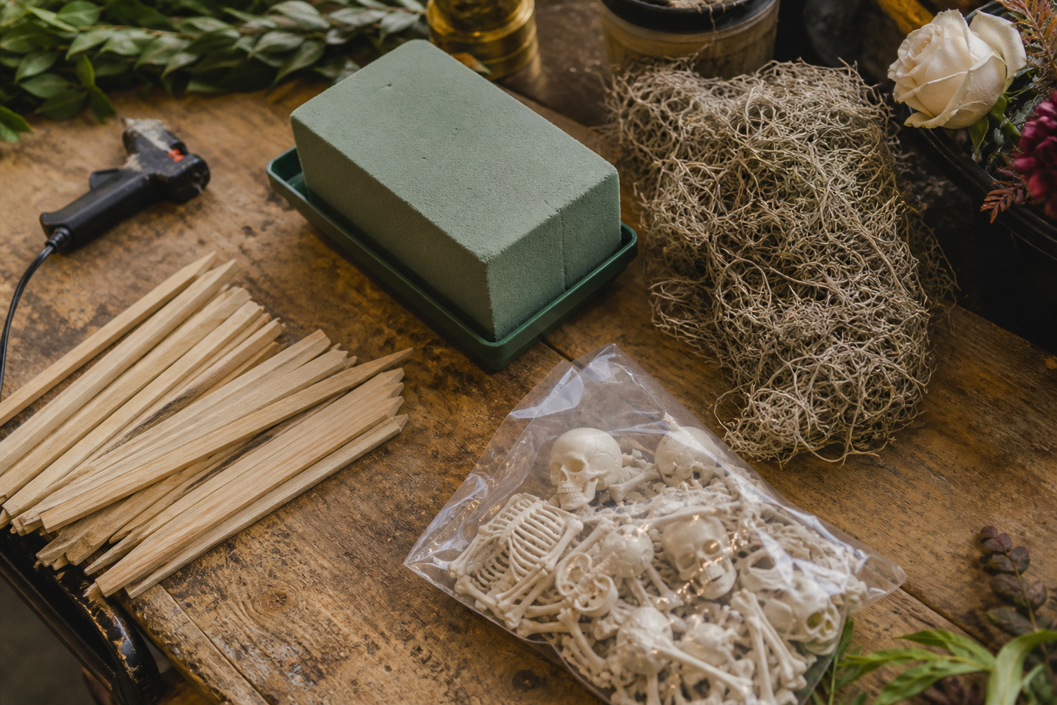 Floral foam, wood stakes, glue gun, and a bag of resin skull and bones laid out on a worktable