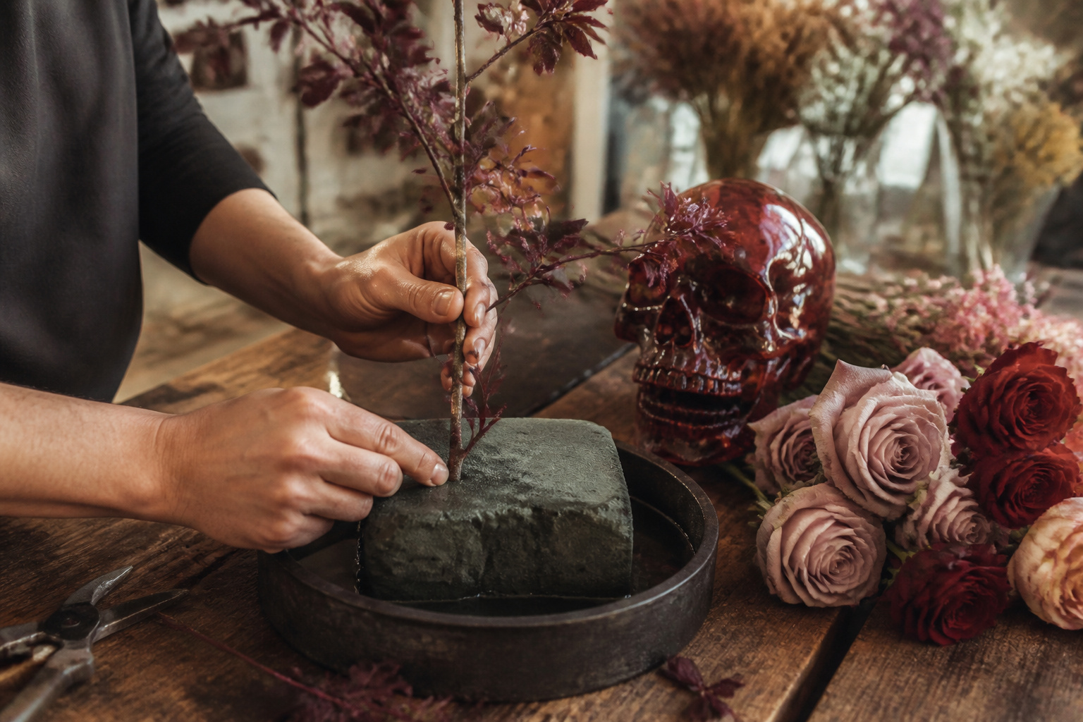Florist hands arranging plum branches and a resin skull into floral foam
