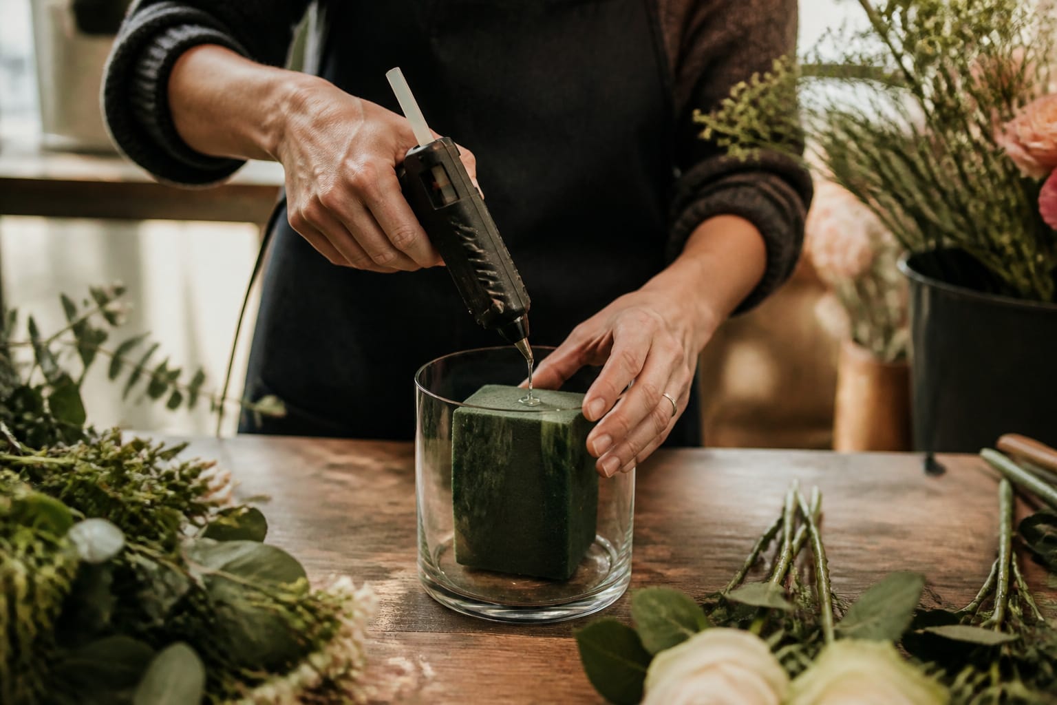 Florist applying pan melt glue to secure floral foam inside a vase