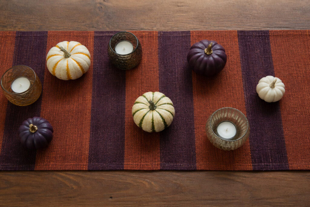 Rust-orange and eggplant-purple striped table runner styled with mini pumpkins and candle holders