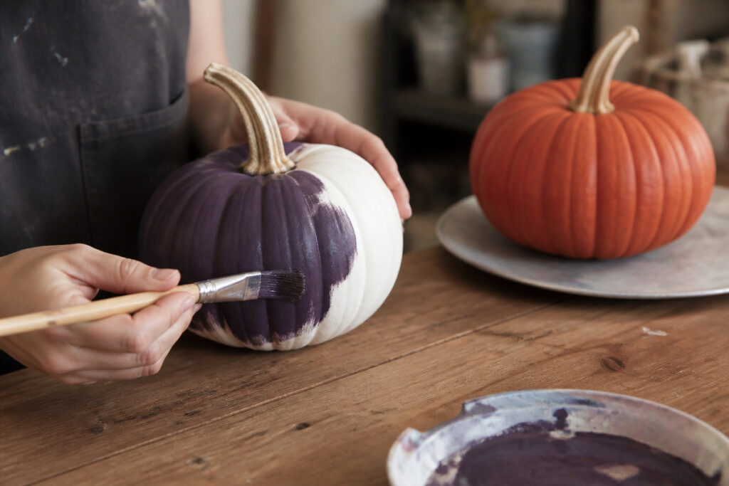 Florist hand-painting a white pumpkin matte eggplant purple with a small brush