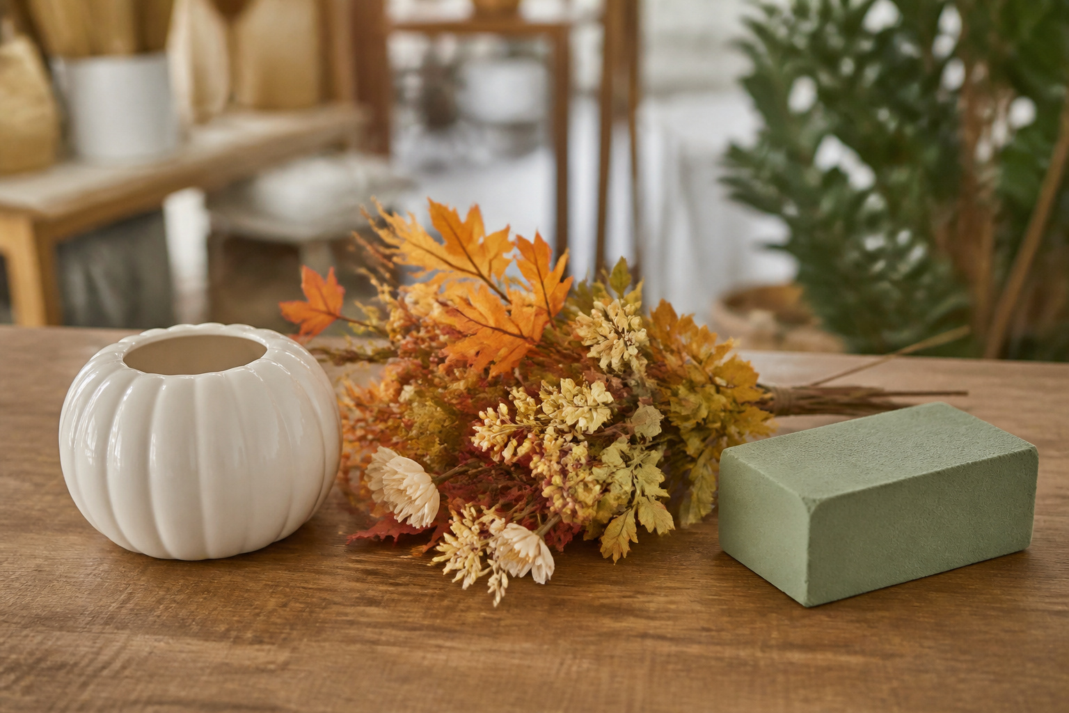 Ceramic pumpkin vase, faux fall stems, and floral foam laid out as budget picks